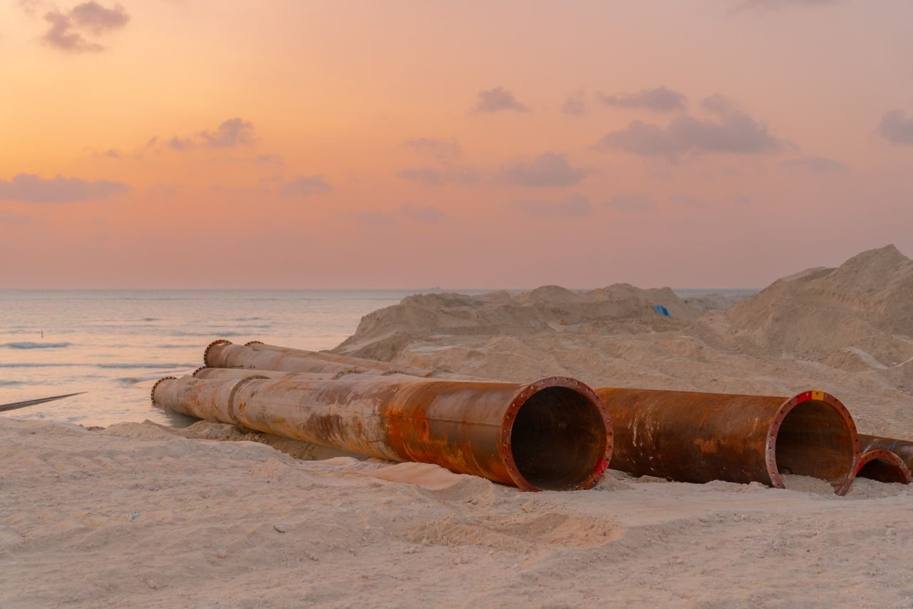Rusty pipes at a coastal construction site with scenic sunset view.