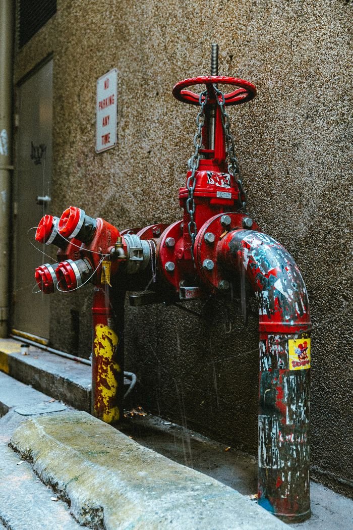 Rustic red fire hydrant with peeling paint in urban alleyway.